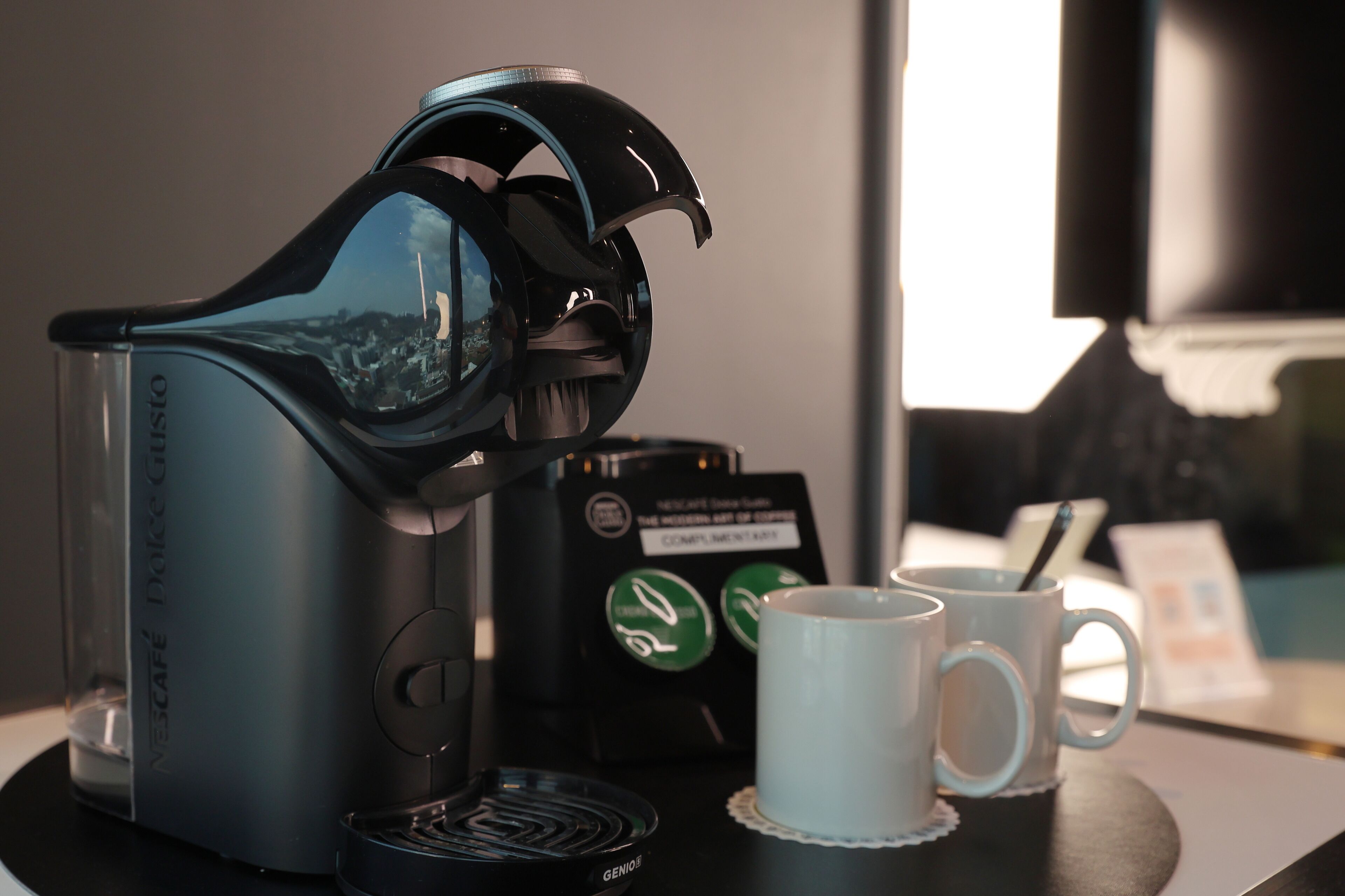 A Nescafé Dolce Gusto coffee machine with two white cups on a table.