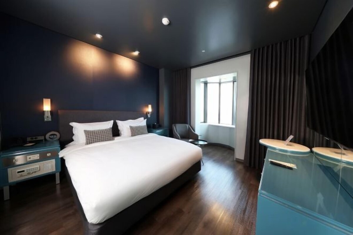 A modern hotel room with a large bed, bedside tables, a desk, and a window with curtains.