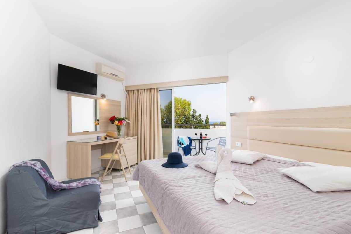 A hotel room with a bed, a desk, a chair, a TV, and a balcony with a table and chairs.