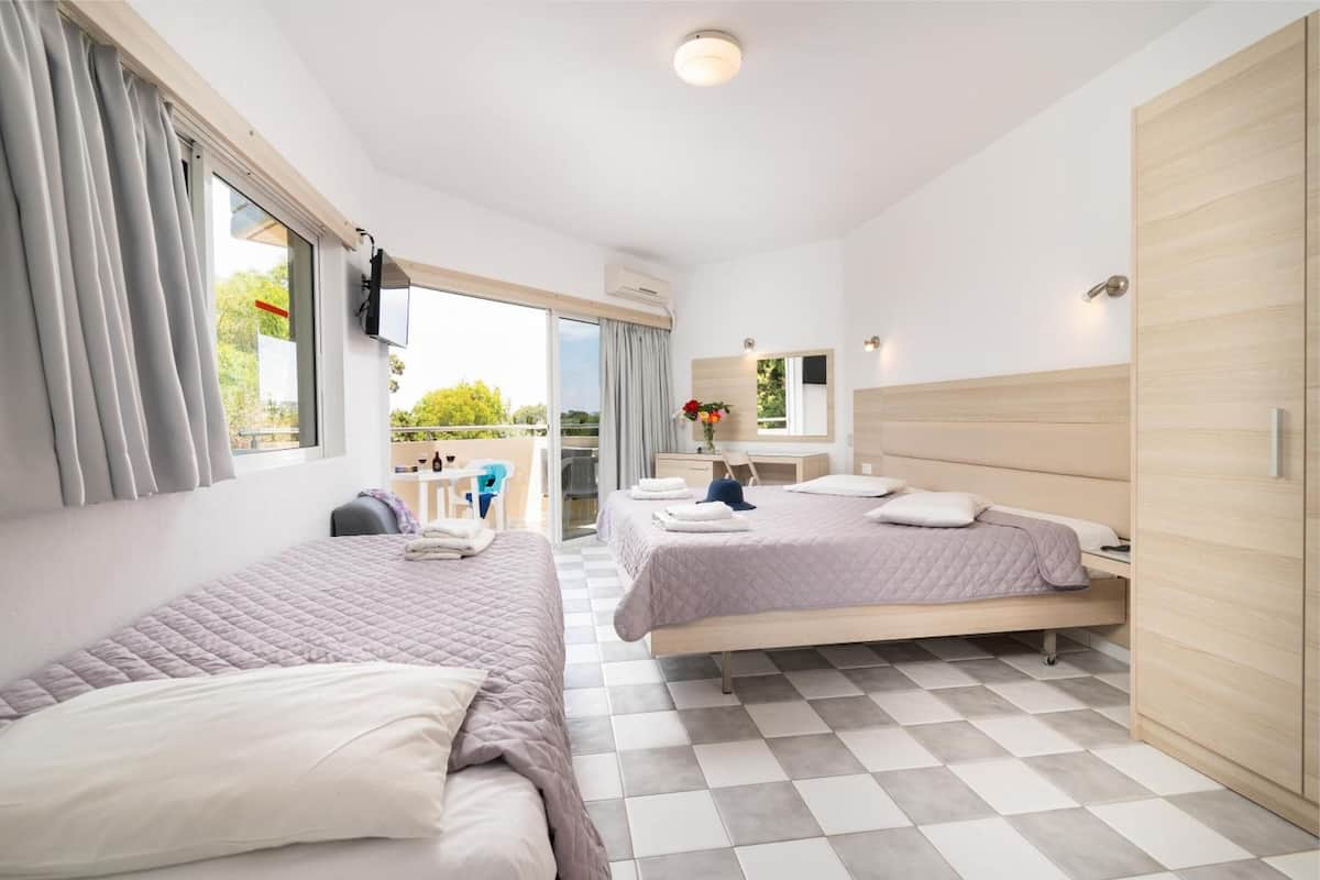 A hotel room with two beds, a balcony, a desk, and a wardrobe.