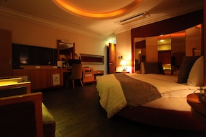 A hotel room with a bed, a desk, a chair, a television, and a mirror. - Bellagio Hotel (Pyeongtaek)