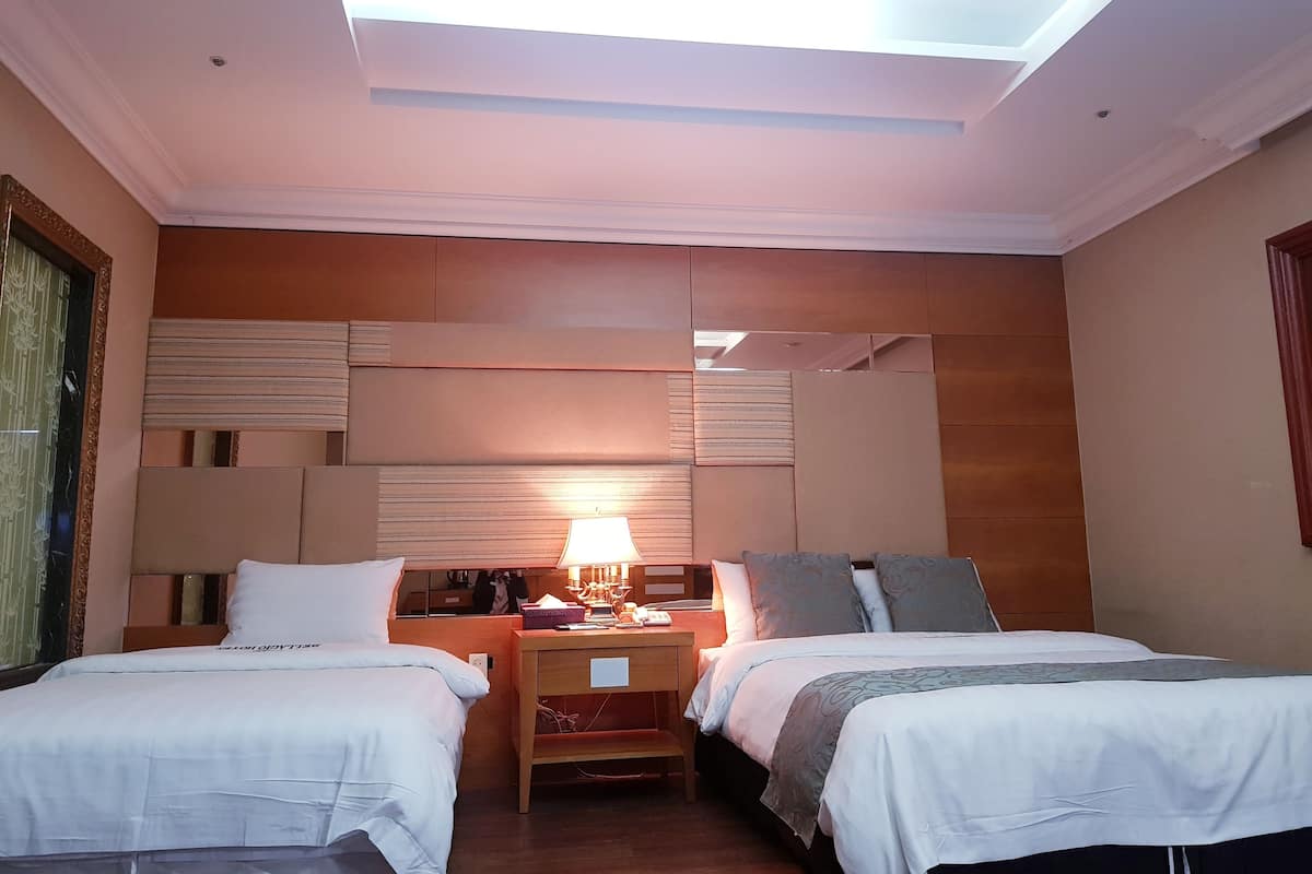 A hotel room with two beds, a nightstand, a lamp, and a skylight.
