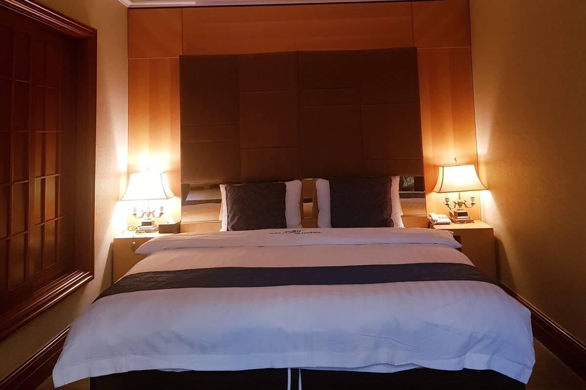 A hotel room with a large bed, two bedside lamps, and a circular ceiling light.