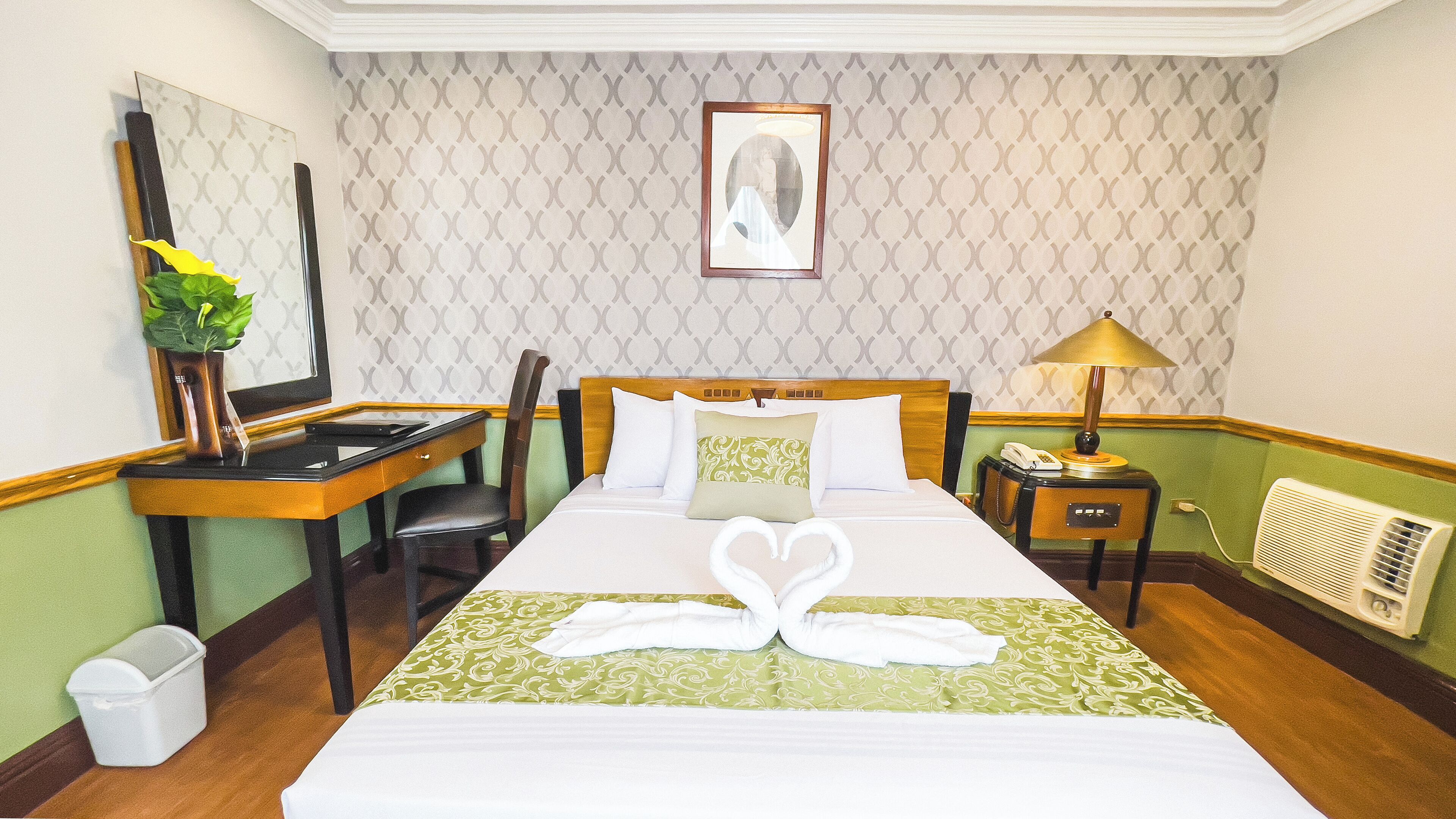 A hotel room with a bed, a desk, a chair, a lamp, and a picture on the wall.