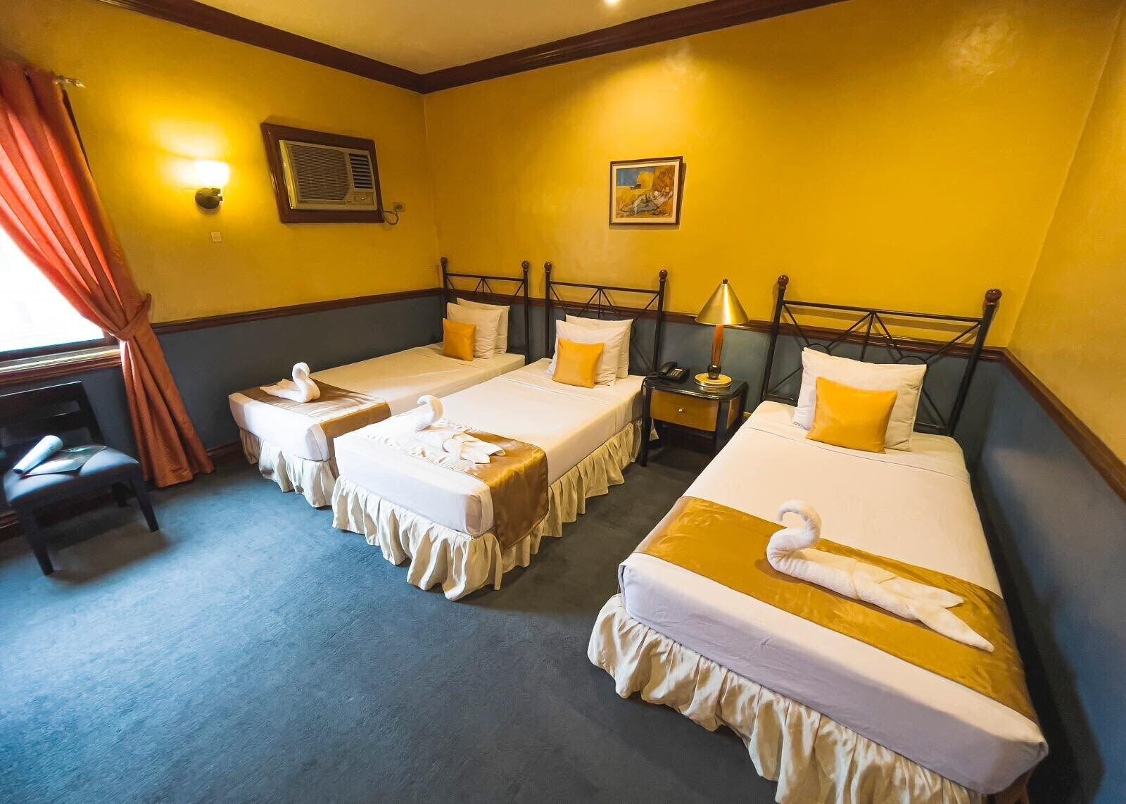Une chambre d’hôtel avec deux lits simples, un bureau avec une chaise, une table de chevet et une lampe.