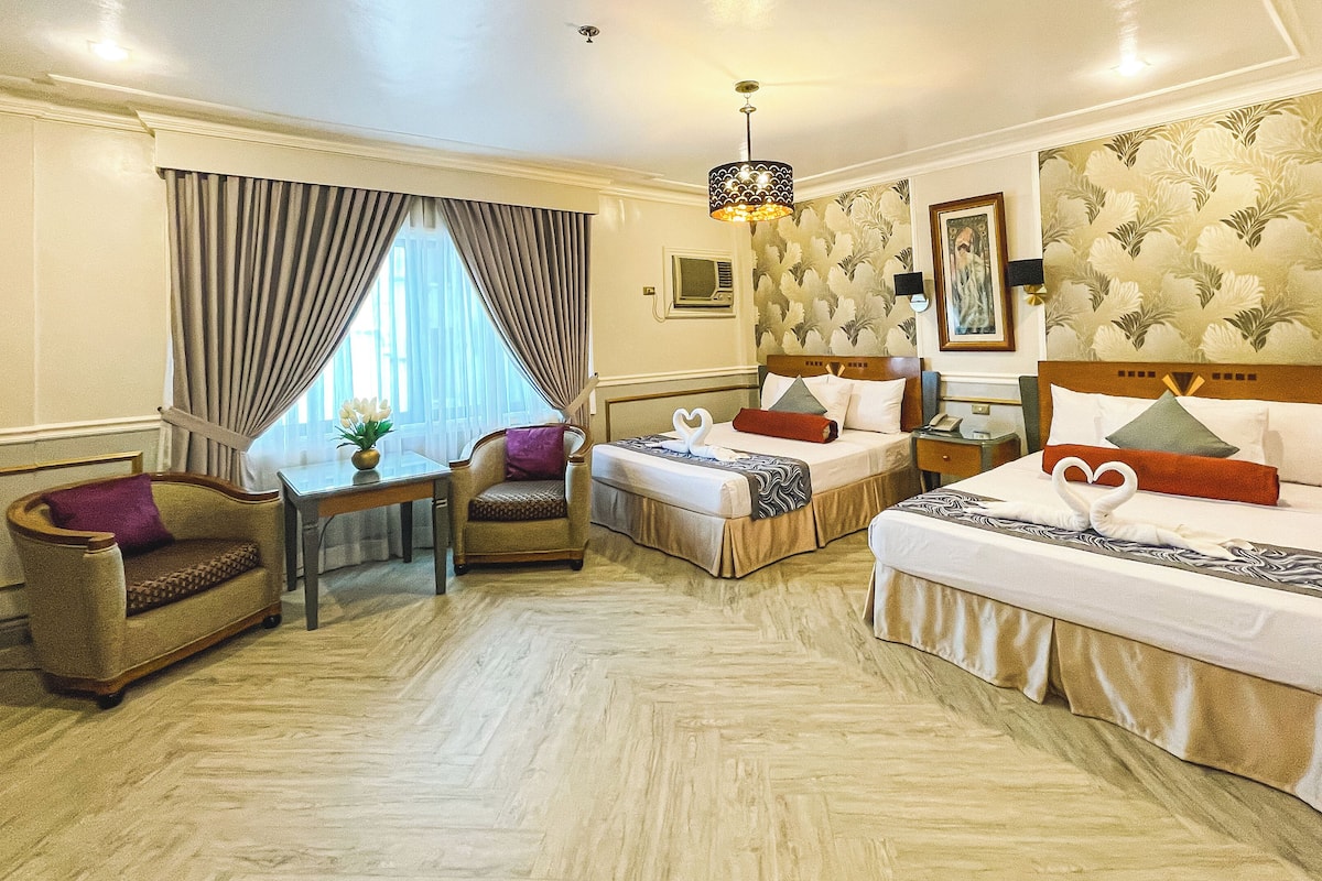A hotel room with two beds, a sofa, a small table, and a chair.