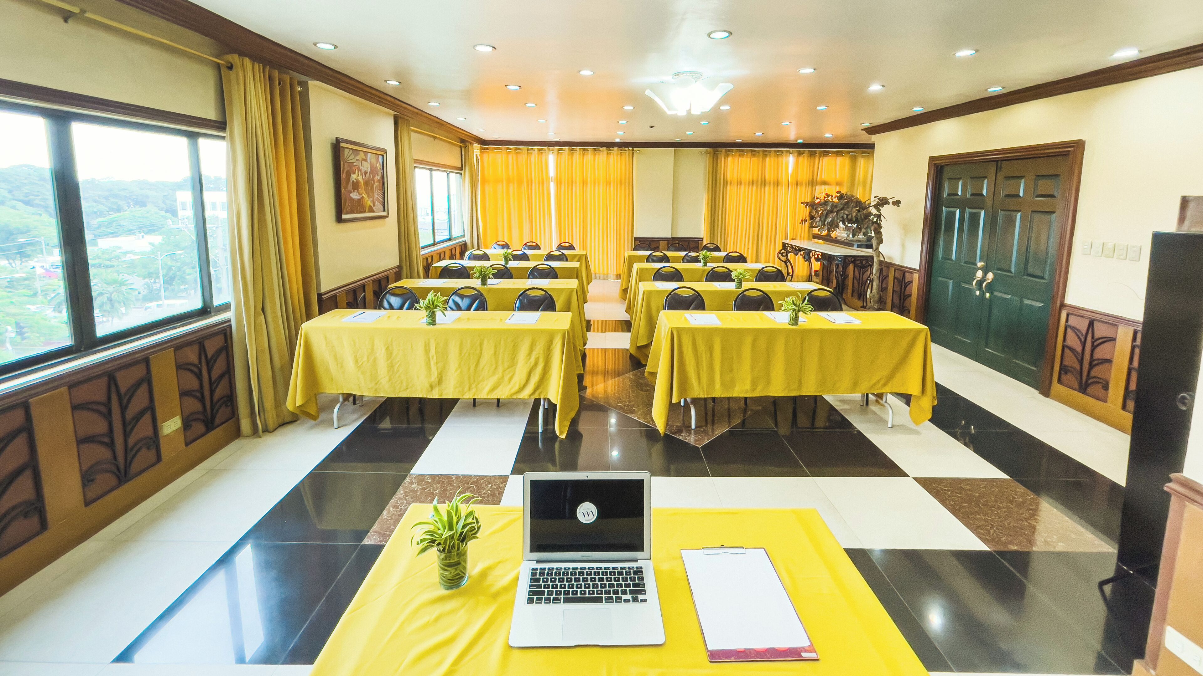 Un salón de conferencias con mesas amarillas, una computadora portátil y una planta sobre un mantel amarillo.