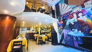 A restaurant with multiple dining areas, a mural on the wall, and a staircase leading to an upper level. - Miramar Hotel (Manila)