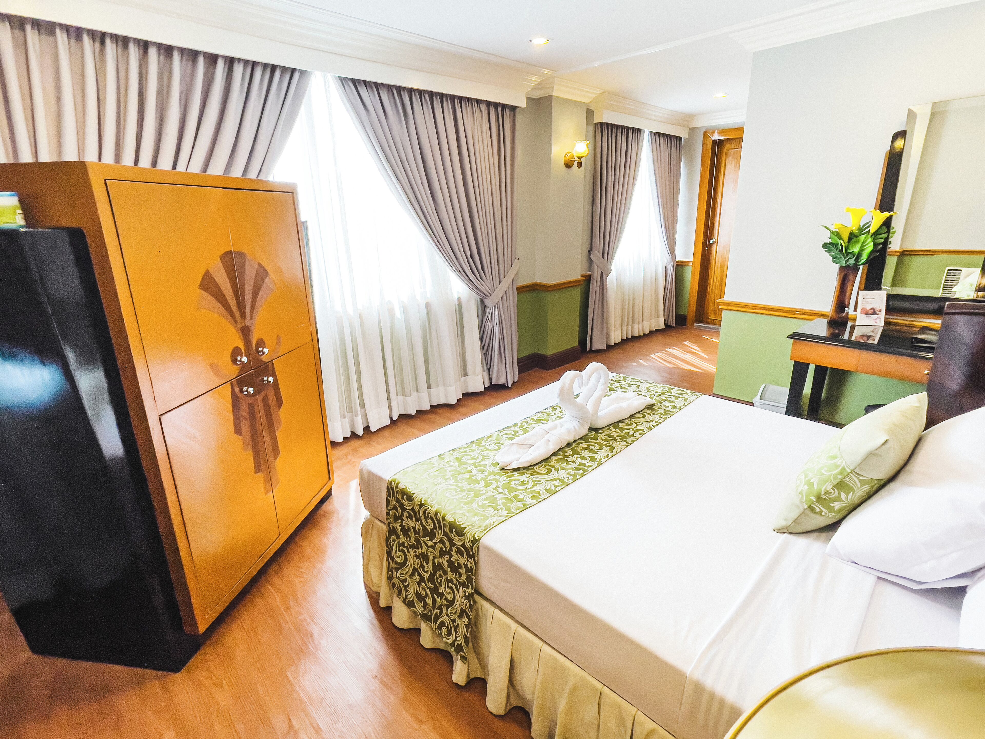 Habitación de hotel con cama, armario, escritorio con espejo y ventana con cortinas.