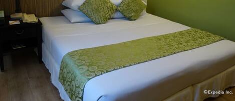 A neatly made bed with green patterned pillows and a green bedspread, a bedside lamp, a phone, and a framed painting on the wall.