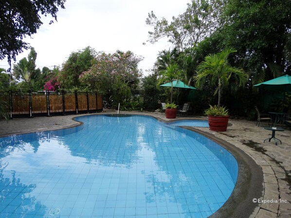 Una piscina con bordes de azulejos, rodeada de plantas en macetas y mobiliario de exterior.