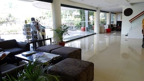 A spacious lobby with a modern design, featuring a seating area with sofas and a coffee table, a large potted plant, and a staircase leading to an upper level. - Hotel Fleuris Palawan (Puerto Princesa)