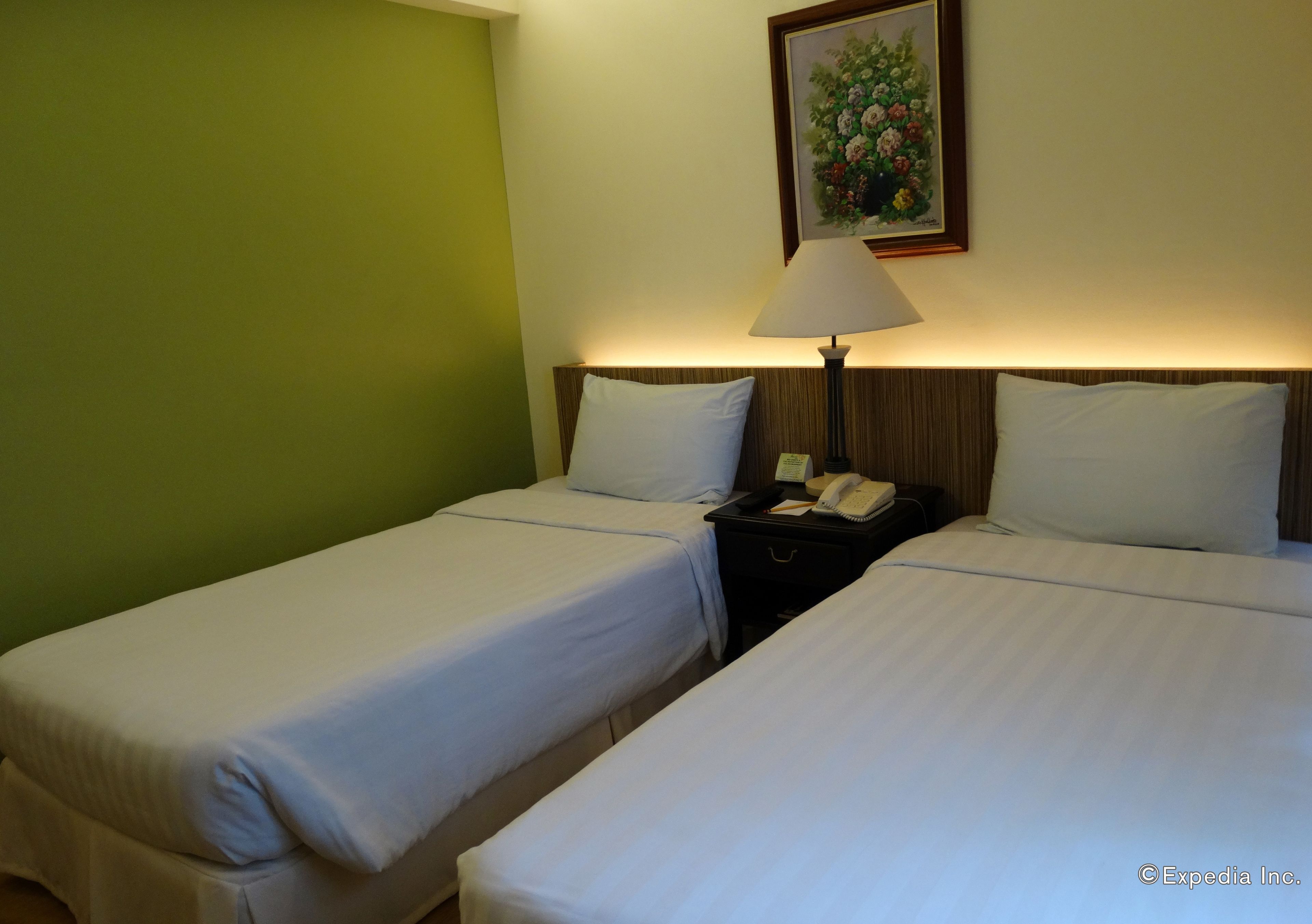 A hotel room with two single beds, a nightstand with a lamp, and a painting on the wall.