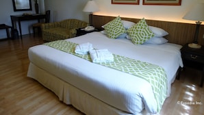 A hotel room with a large bed, two pillows, a bedside table with a lamp, a chair, a desk, and two paintings on the wall. - Hotel Fleuris Palawan (Puerto Princesa)