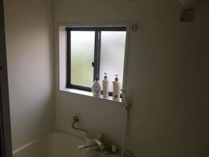 A small bathroom with a window, a toilet, and a shower.