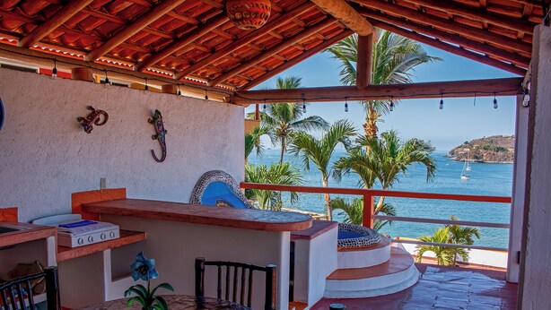 Un espacio de estar al aire libre cubierto con vistas al mar, que incluye una mesa, sillas y un muro decorativo.