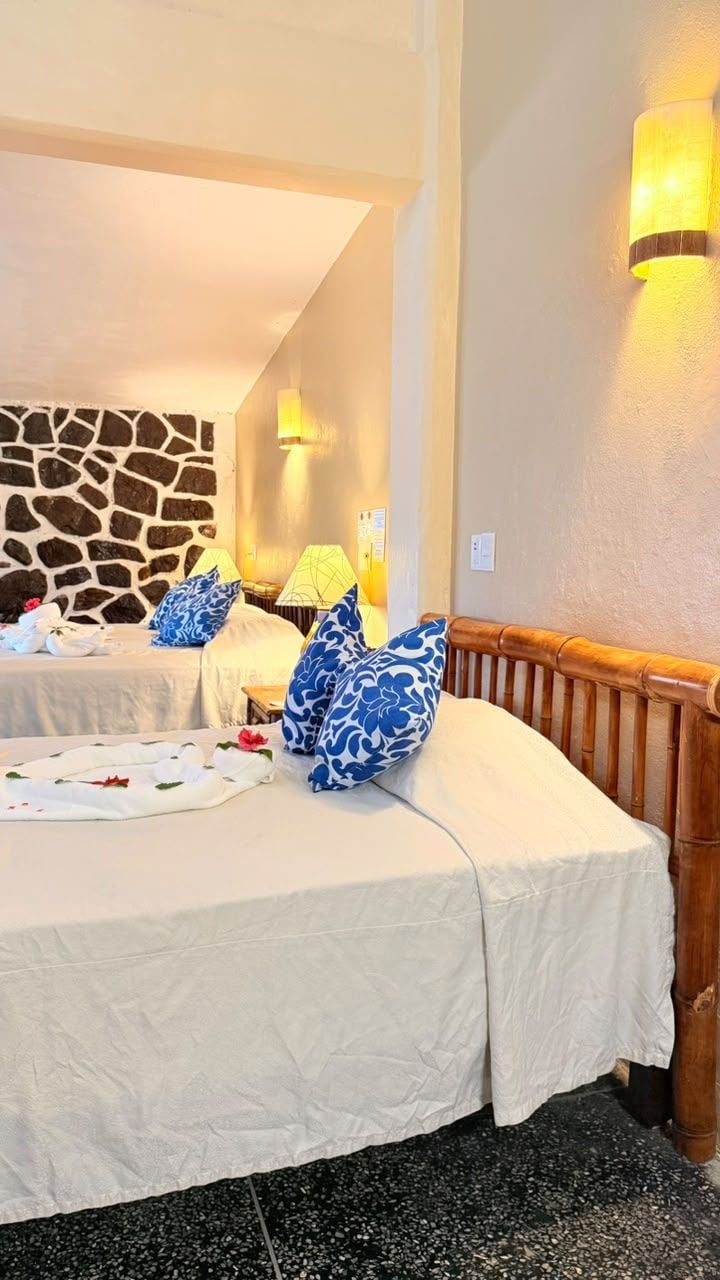 A hotel room with two beds, a stone wall, and a wooden headboard.