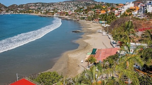 Un pueblo costero con playa, casas y una colina al fondo.