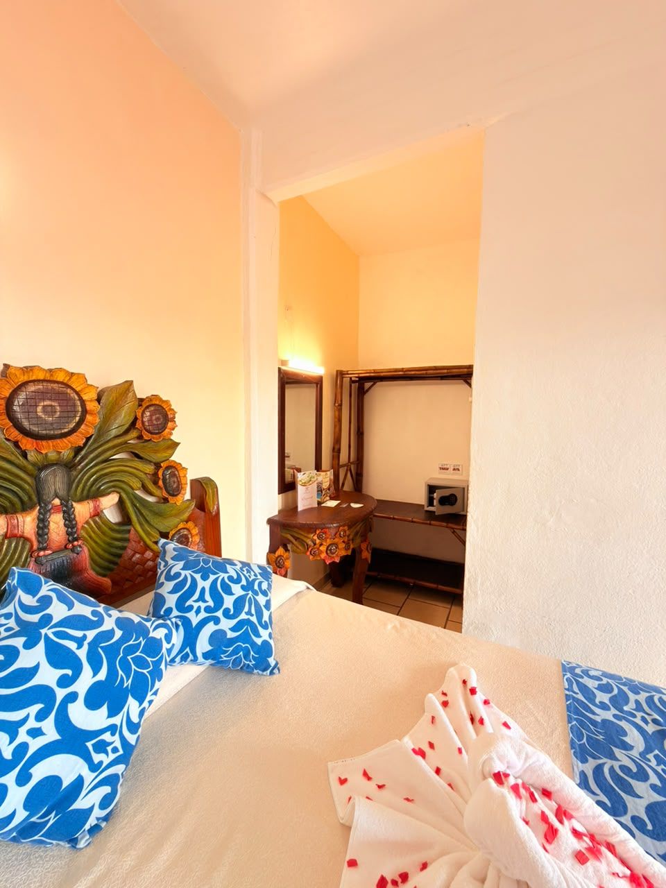 A hotel room with a bed, a wooden headboard with a floral design, a bedside table, and a mirror.