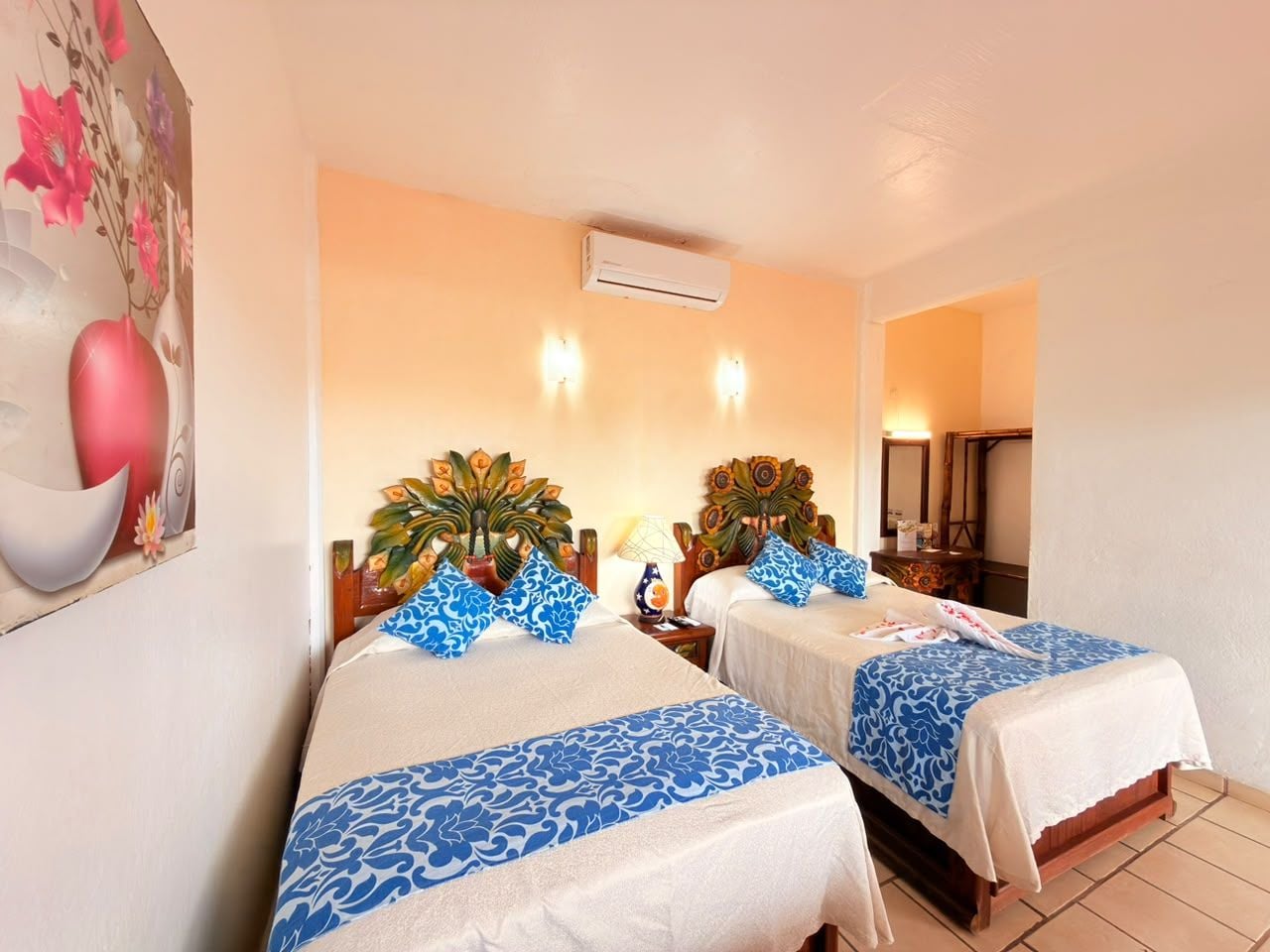 A hotel room with two beds, a nightstand, a lamp, and a wall-mounted air conditioner.