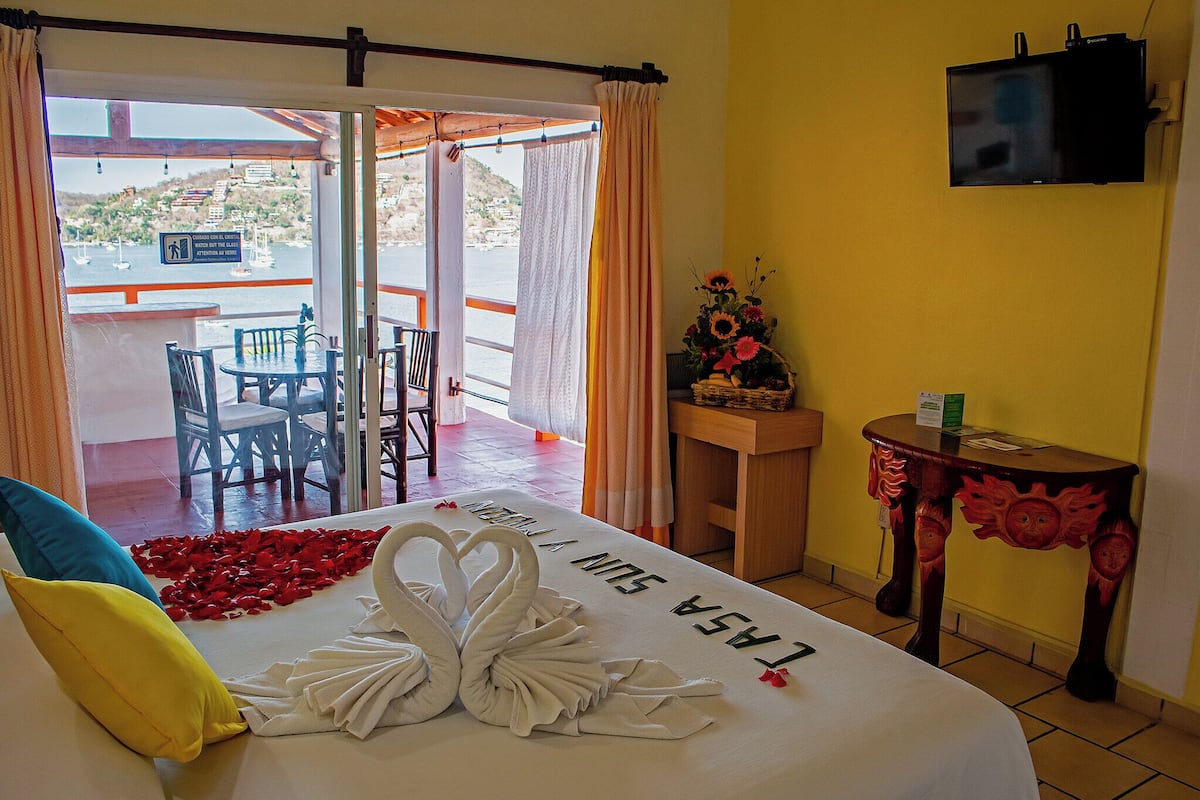 A hotel room with a bed, a TV, a table with a vase, and a view of the sea.