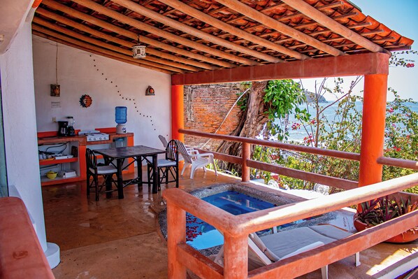 A covered outdoor area with a pool, a table with chairs, and a view of the sea.