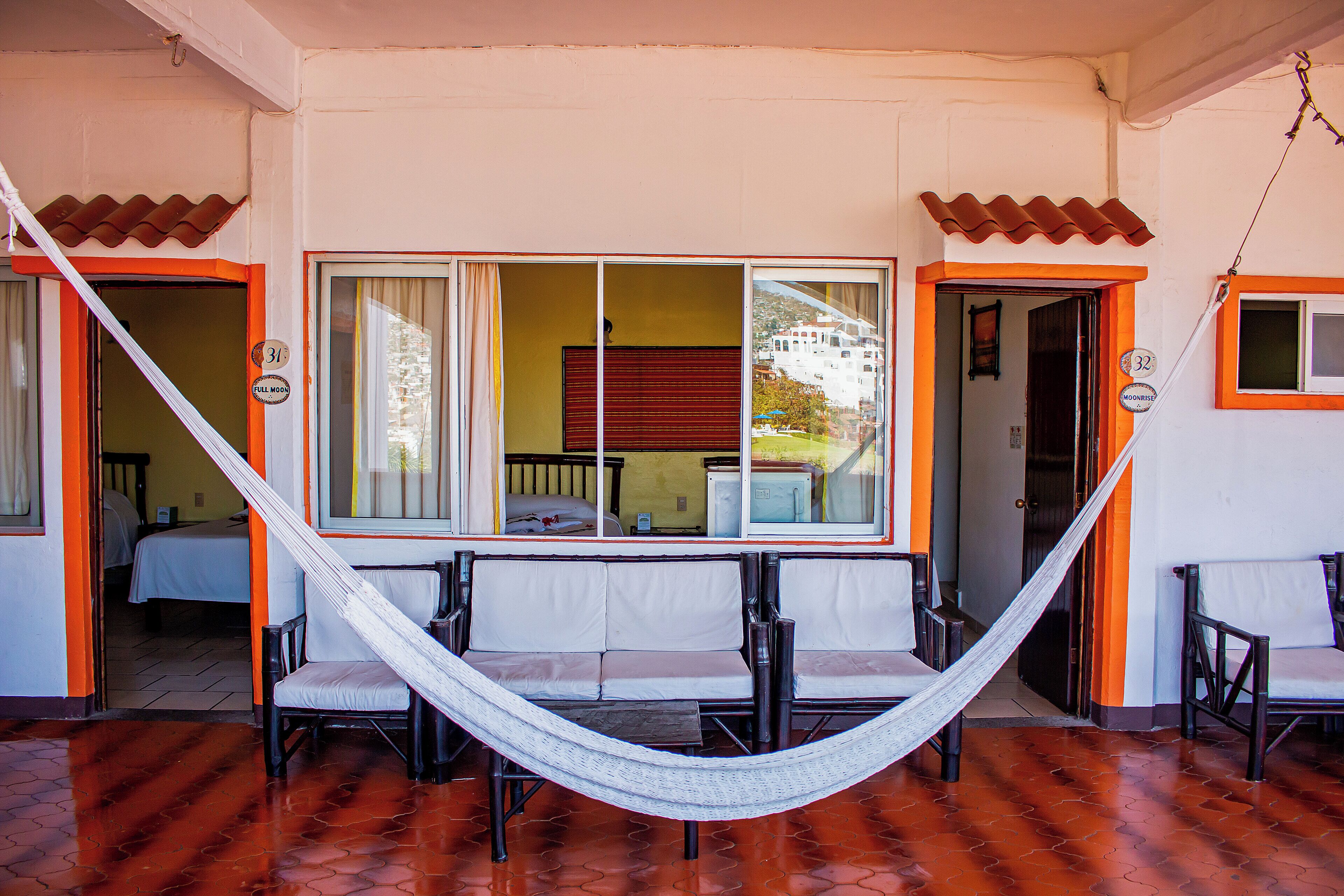 Quarto com rede, duas cadeiras, cama e janela com cortinas.