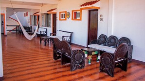 Un comedor con mesa y sillas de madera, una hamaca y piso de baldosas.