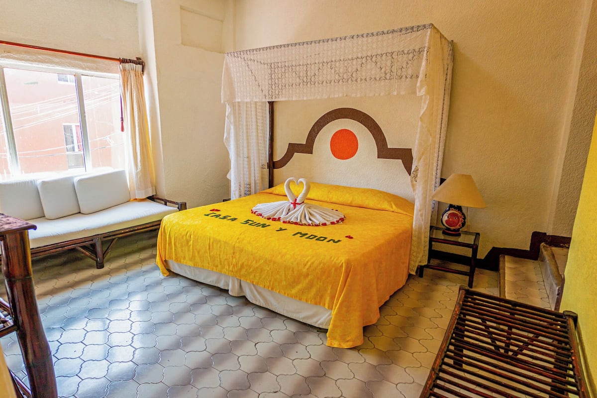 A bed with a yellow bedspread, a canopy, and a decorative pillow with a heart.