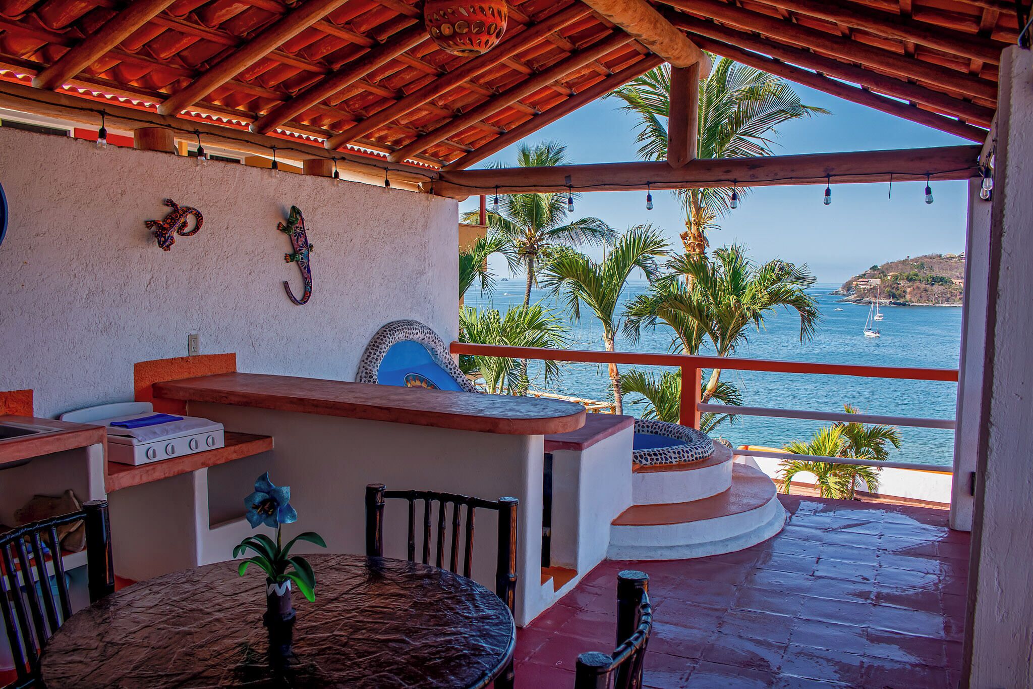 Un'area salotto esterna coperta con vista sul mare, un bar e un muro decorativo.