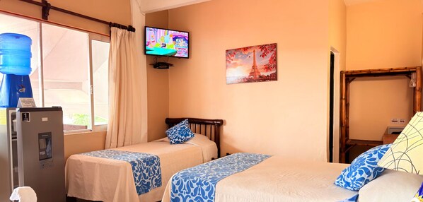 A hotel room with two beds, a television, a painting of the Eiffel Tower, and a water dispenser. - Casa Sun and Moon (Zihuatanejo)