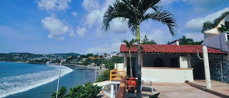 Una propiedad costera con vista al mar, una palmera y un edificio con techo de tejas rojas.
