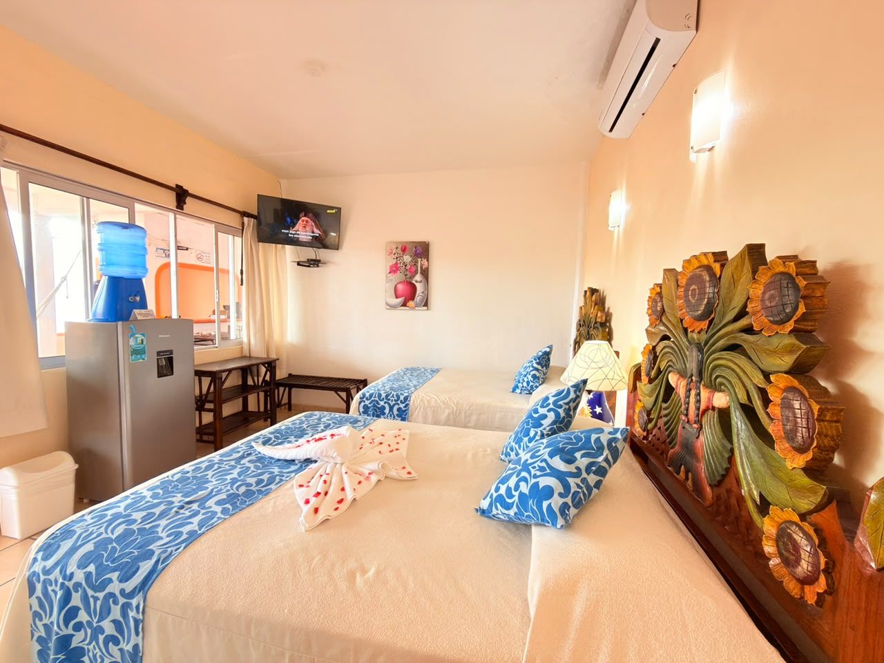 Habitación de hotel con dos camas, televisor, refrigerador, mesa y un adorno de pared.