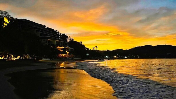 Una playa al atardecer con edificios en el fondo.
