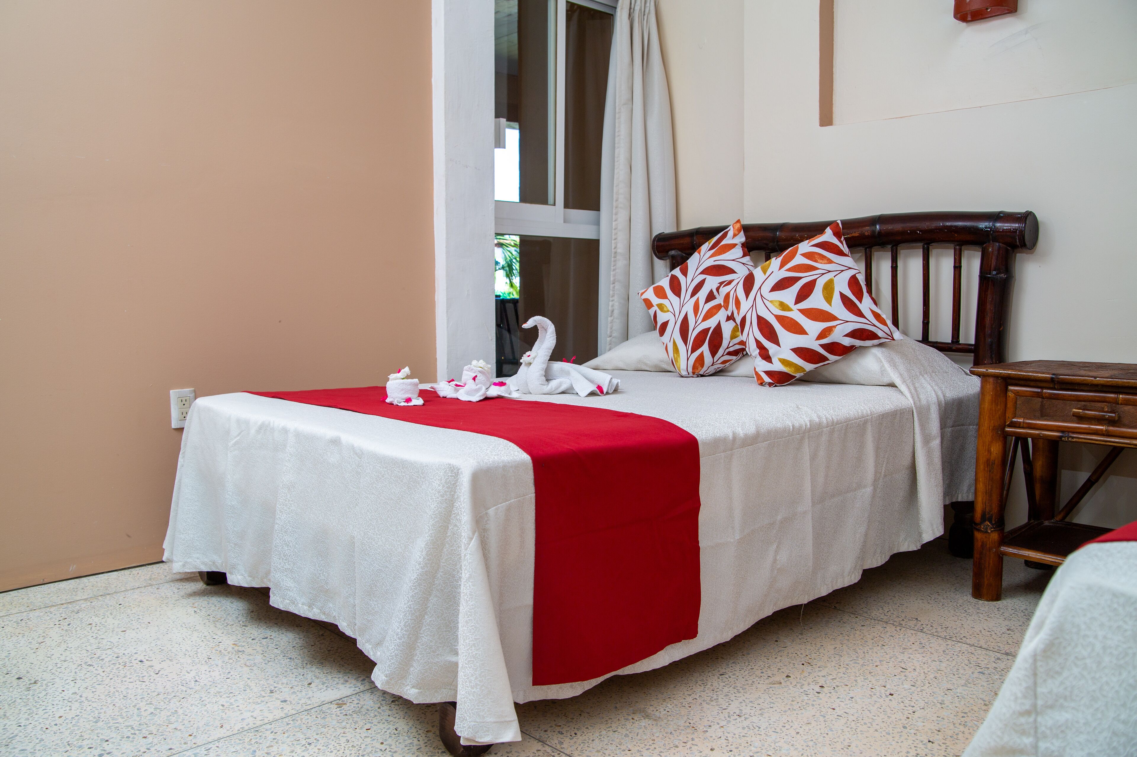 A neatly made bed with a red and white bedspread, two decorative pillows, and a wooden nightstand beside it.