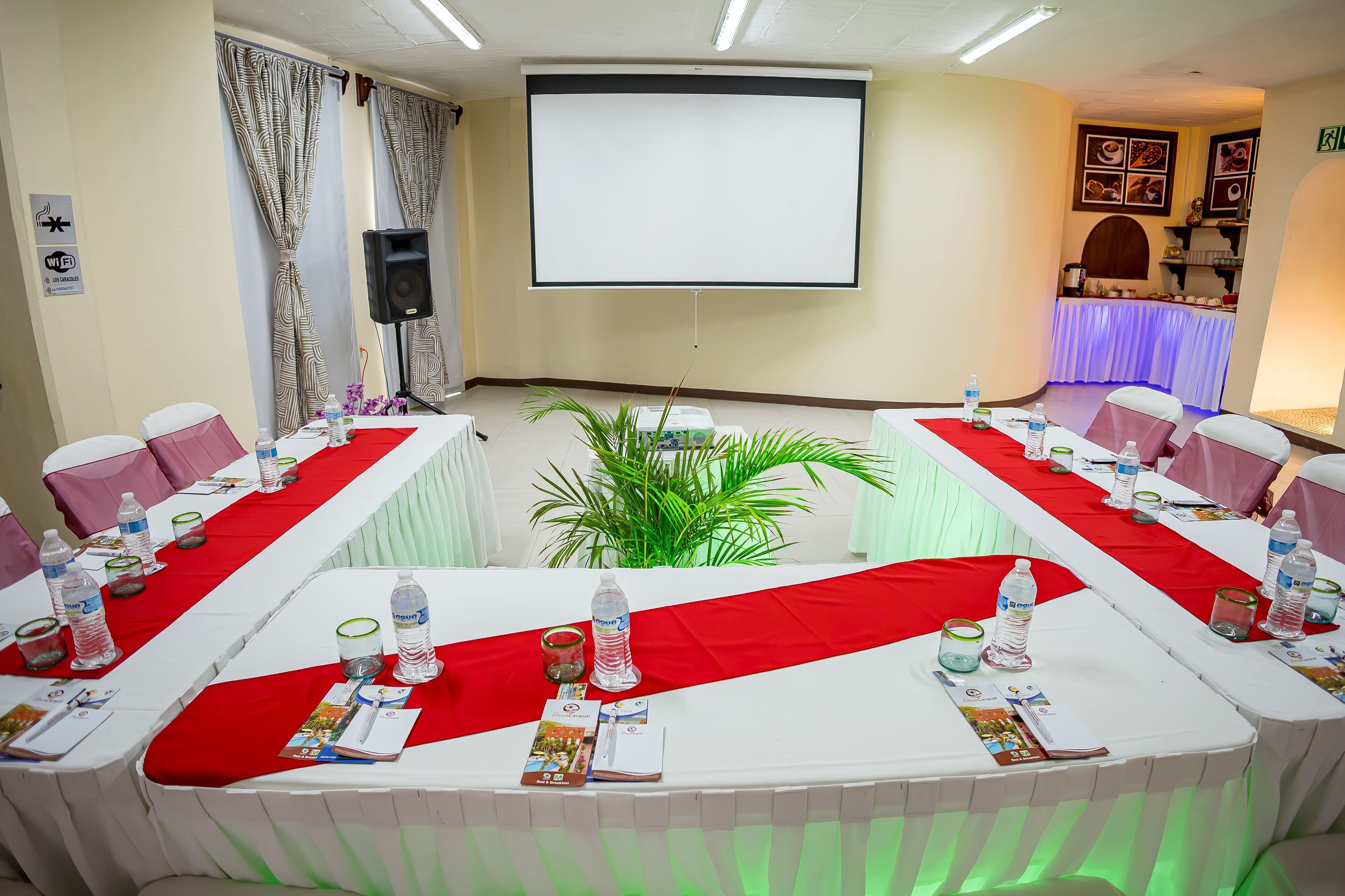 Une salle de conférence équipée d’une grande table, de chaises, d’un écran de projection et d’un espace buffet.