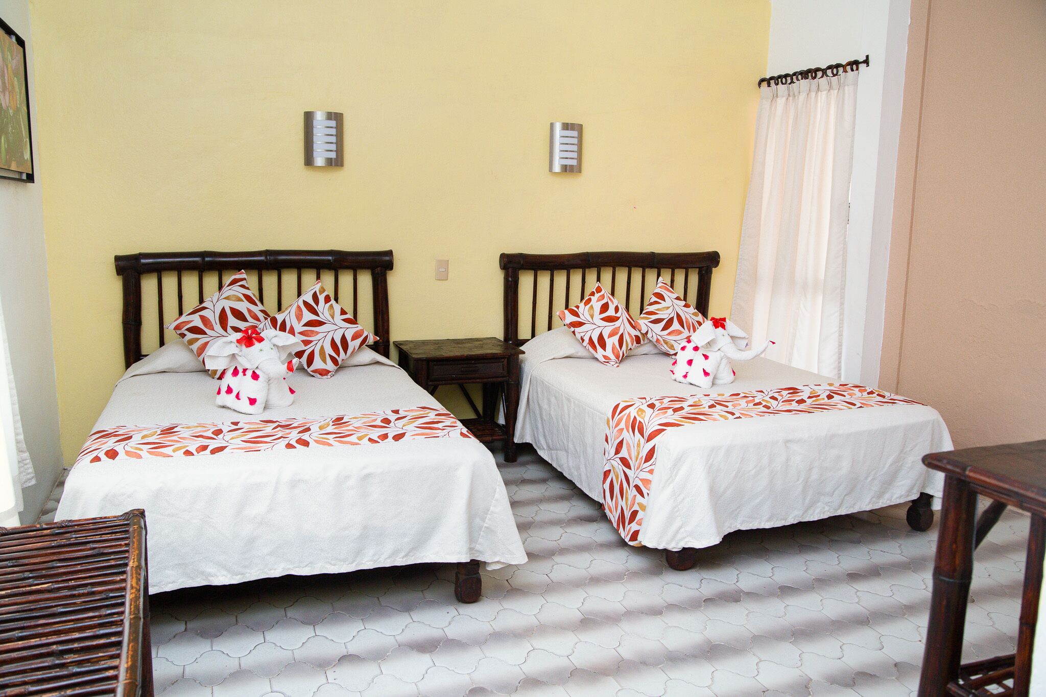 A room with two beds, each with a wooden headboard and white bedding. There are two bedside tables and a small wooden chair.