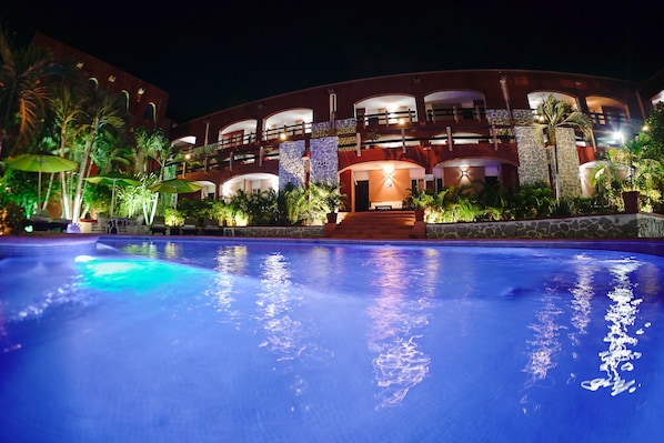 Un hotel con piscina, varios balcones y exuberante vegetación tropical.