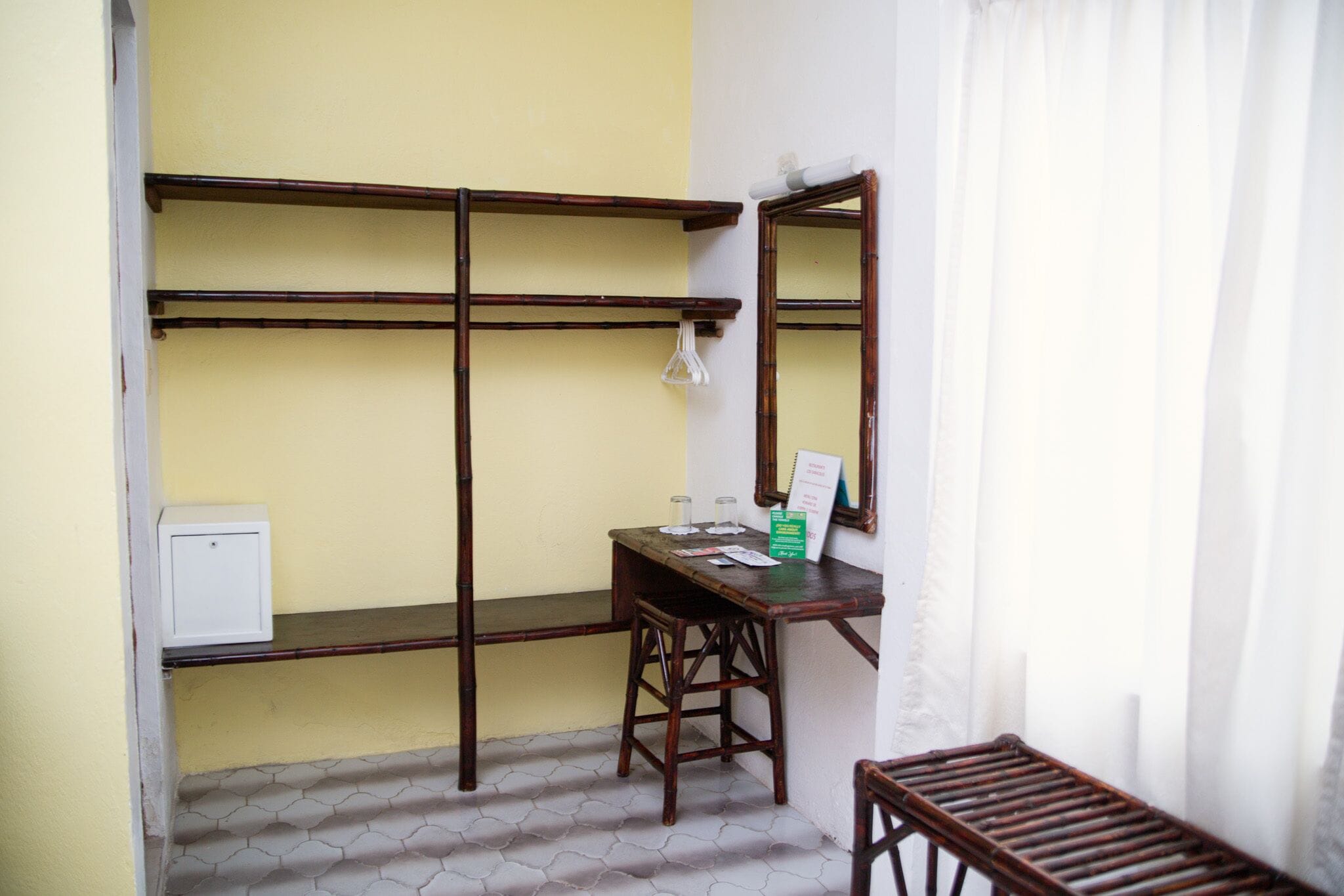 Una habitación pequeña con un escritorio de madera, una silla, un espejo y una estantería frente a una pared amarilla.