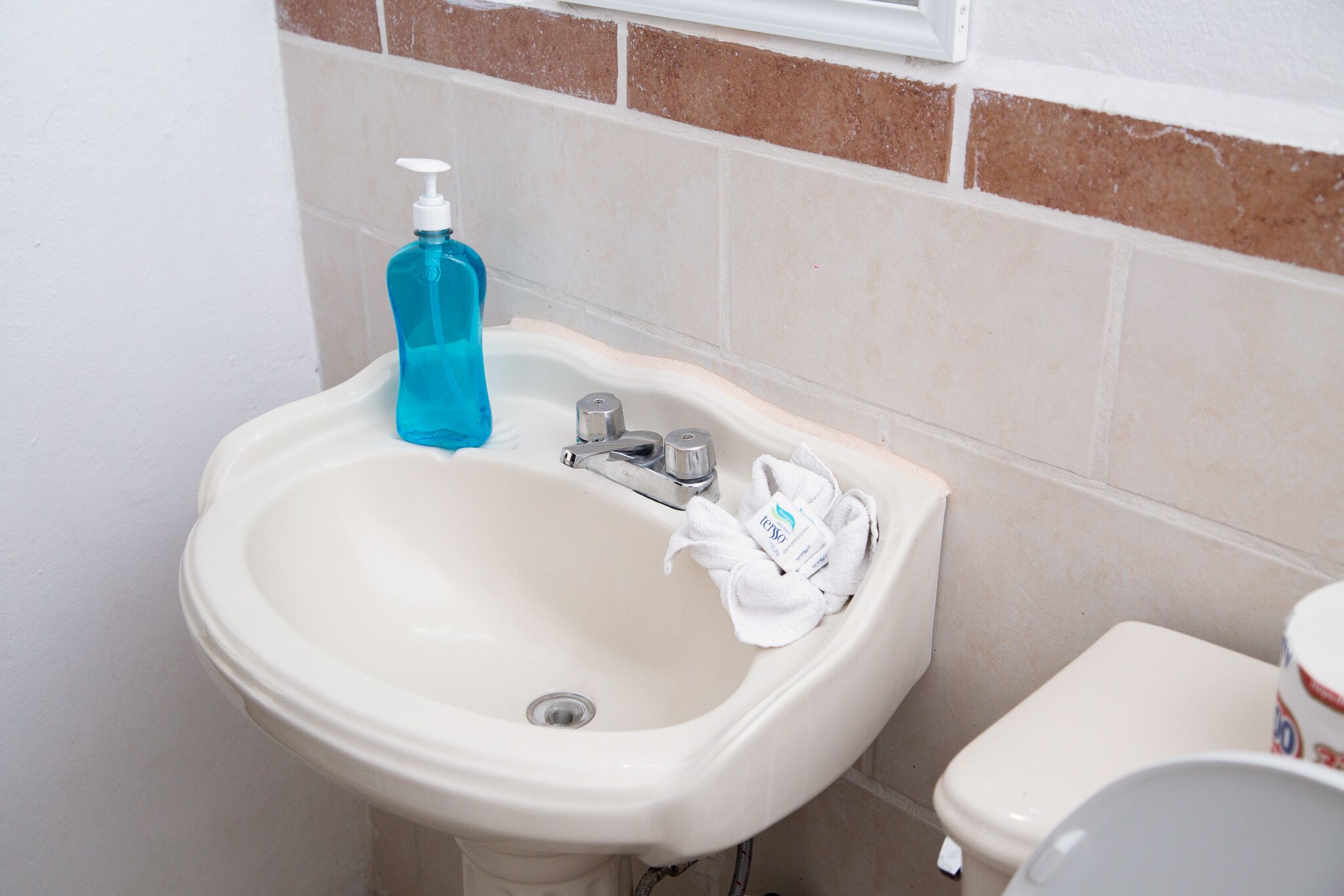 A bathroom sink with a blue soap dispenser, a white towel, and a toilet.