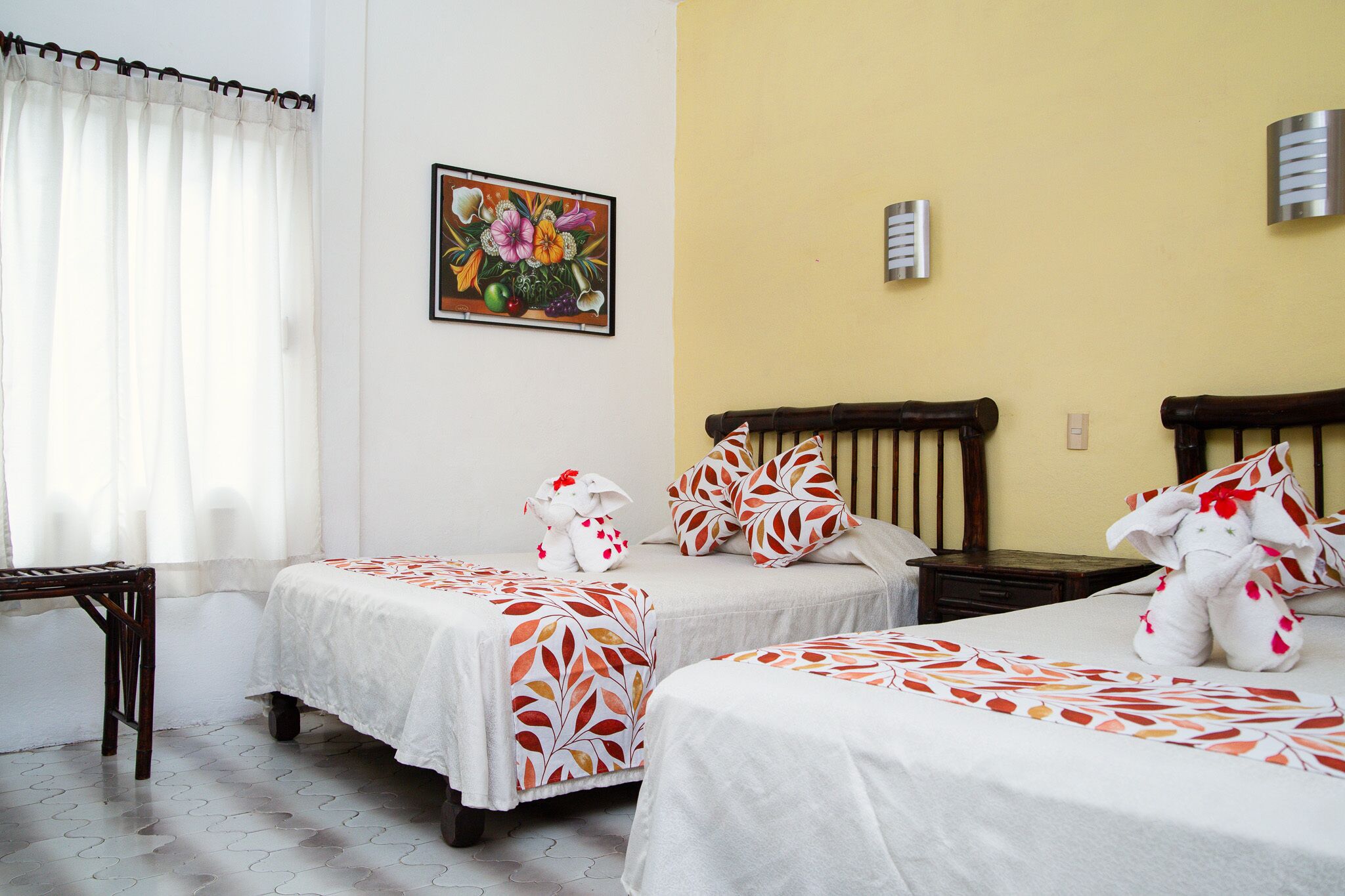 A hotel room with two beds, a wooden nightstand, a small table, and a painting on the wall.