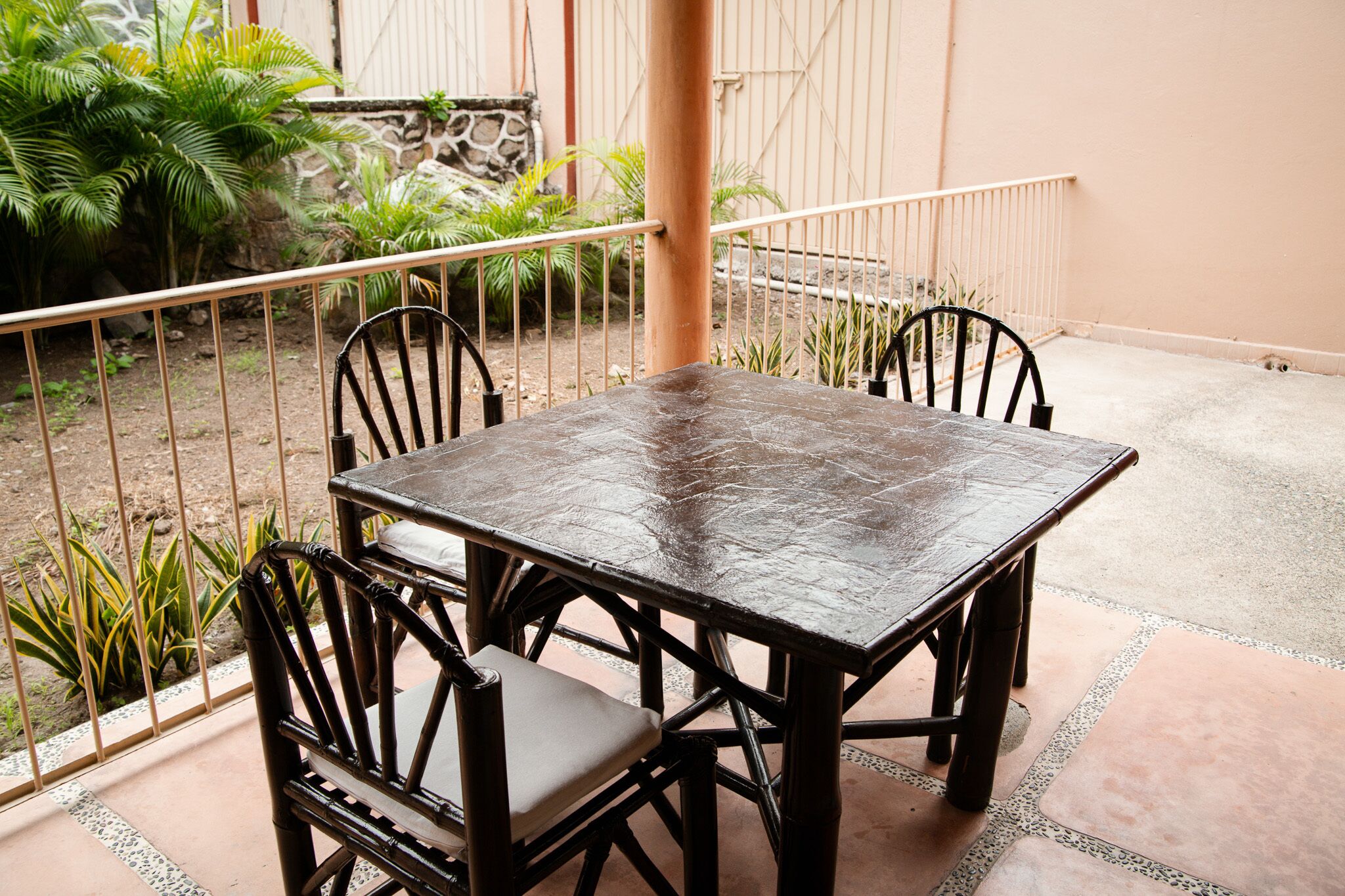 Une table carrée entourée de quatre chaises, une rambarde en métal et, au fond, des plantes en pot.