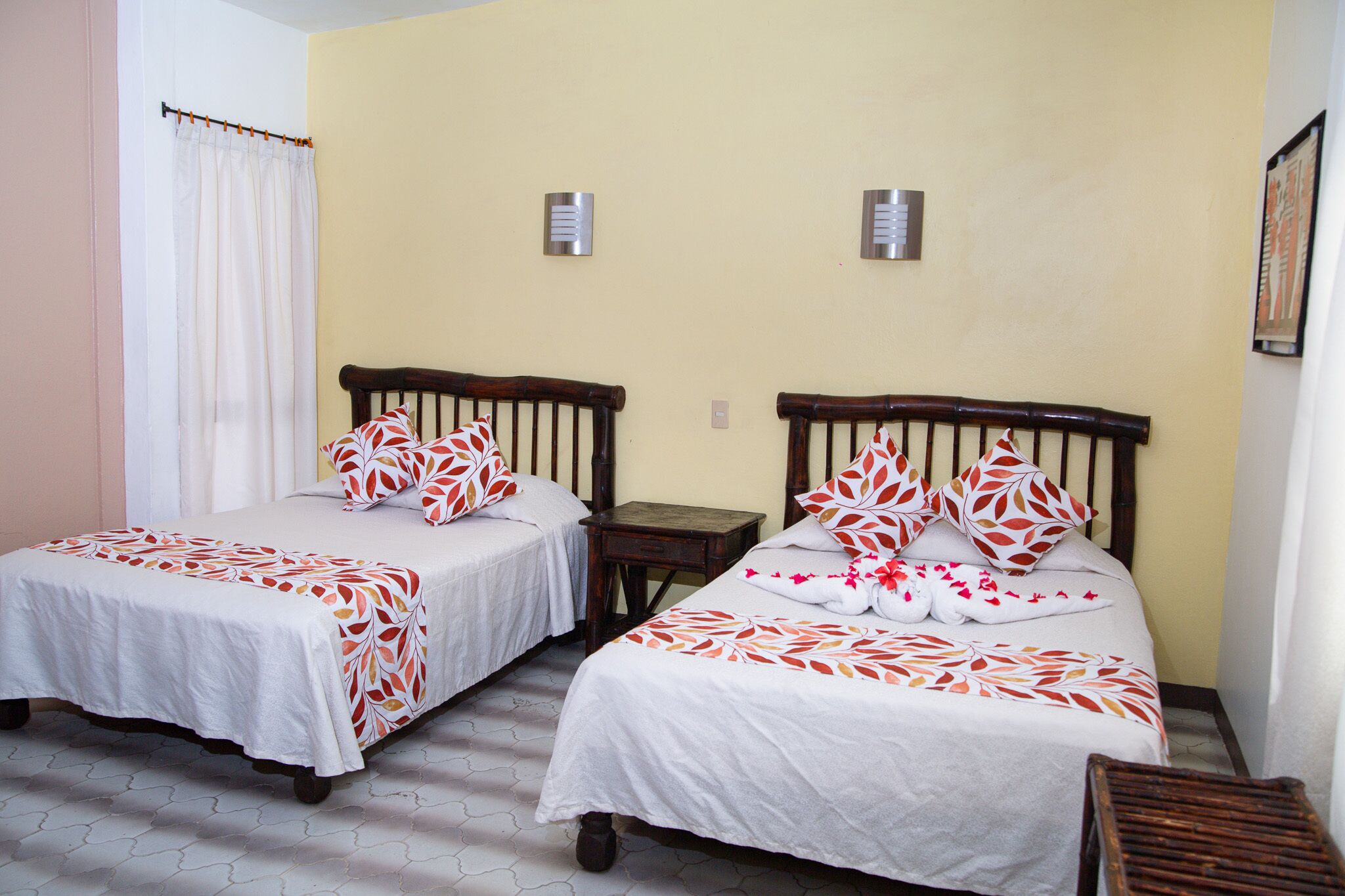 Two single beds with white bedding and red leaf patterns, a wooden nightstand, and a small table between them.