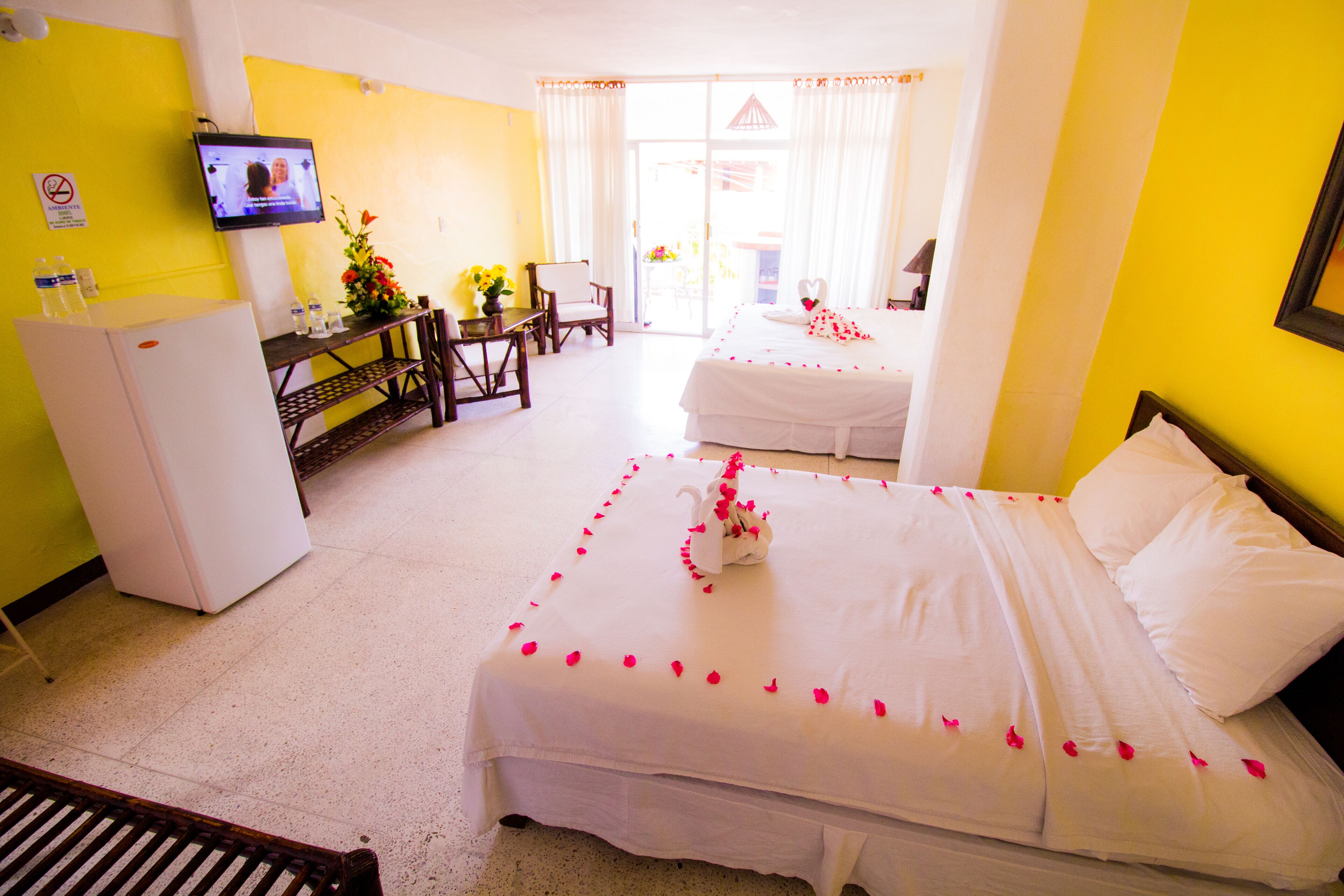 A hotel room with a bed adorned with rose petals, a television on the wall, and a desk with a chair.