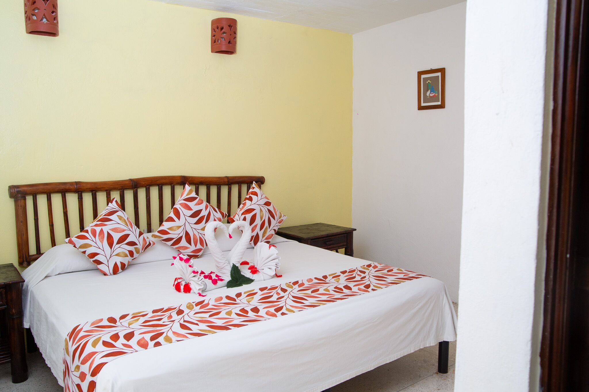 A neatly made bed with a white and orange leaf-patterned bedspread, two wooden nightstands, and a small framed picture on the wall.