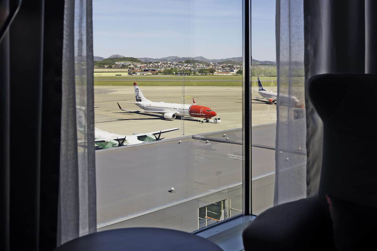 Vista desde el interior de una habitación con un amplio ventanal que da a un aeropuerto.