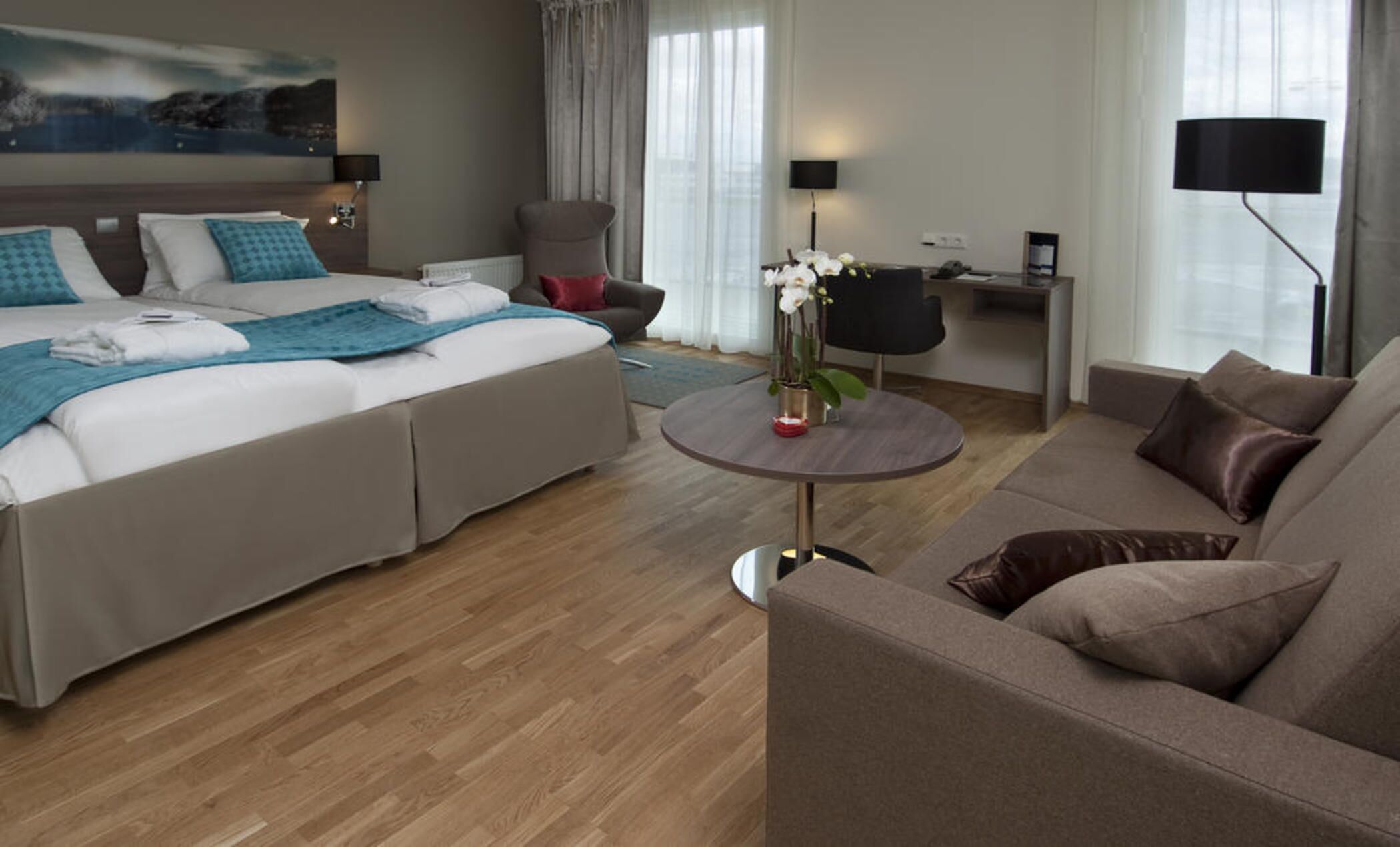 Et hotelværelse med seng, sofa, et lille bord med en vase blomster, et skrivebord med lampe og en stol.