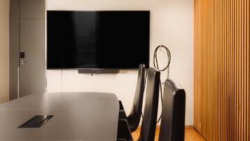 Una sala de conferencias moderna con una gran televisión de pantalla plana en la pared, una mesa elegante y sillas negras.