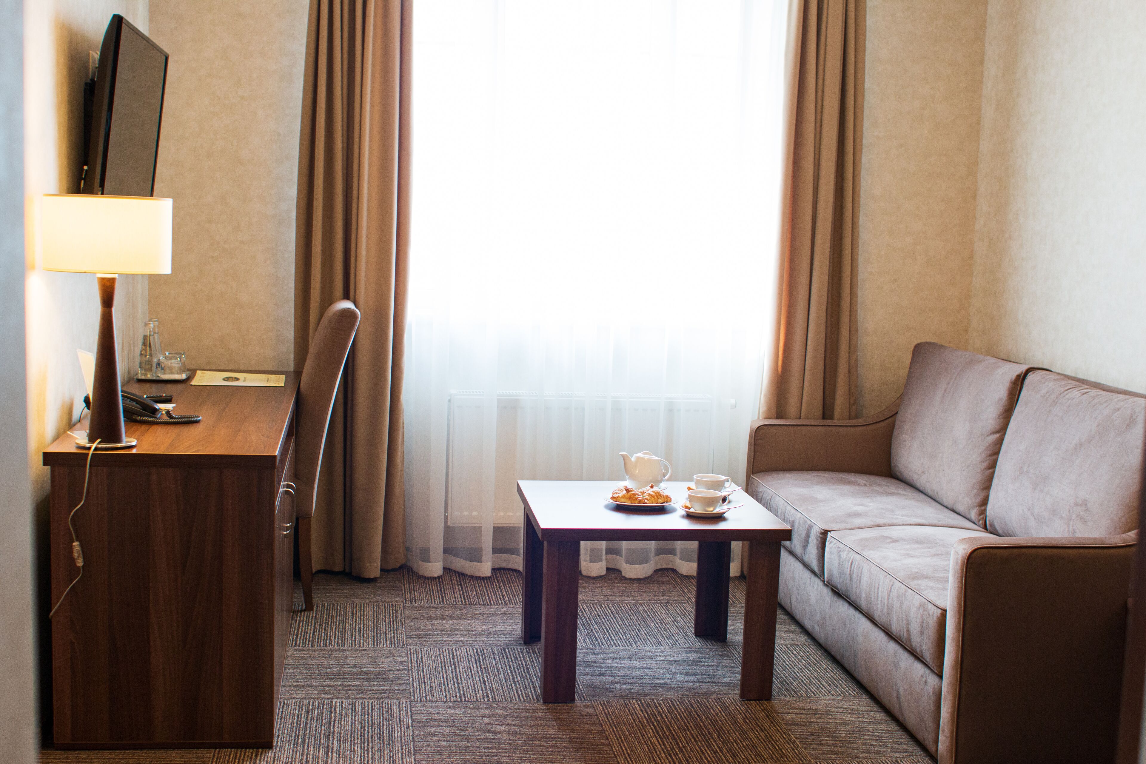 Een hotelkamer met een houten bureau, een televisie, een bank en een kleine tafel met een theepot en kopjes.