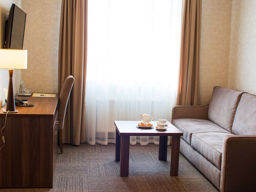 Een hotelkamer met een houten bureau, een televisie, een bank en een kleine tafel met een theepot en kopjes.
